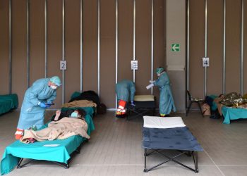 Hospital employees wearing a protection mask and gear tend patients lying in bed at a temporary emergency structure set up outside the accident and emergency department, where any new arrivals presenting suspect new coronavirus symptoms are being tested, at the Brescia hospital, Lombardy, on March 13, 2020. (Photo by Miguel MEDINA / AFP)