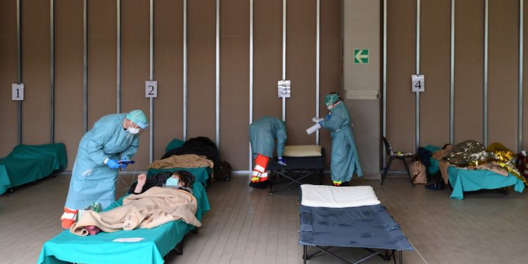 Hospital employees wearing a protection mask and gear tend patients lying in bed at a temporary emergency structure set up outside the accident and emergency department, where any new arrivals presenting suspect new coronavirus symptoms are being tested, at the Brescia hospital, Lombardy, on March 13, 2020. (Photo by Miguel MEDINA / AFP)