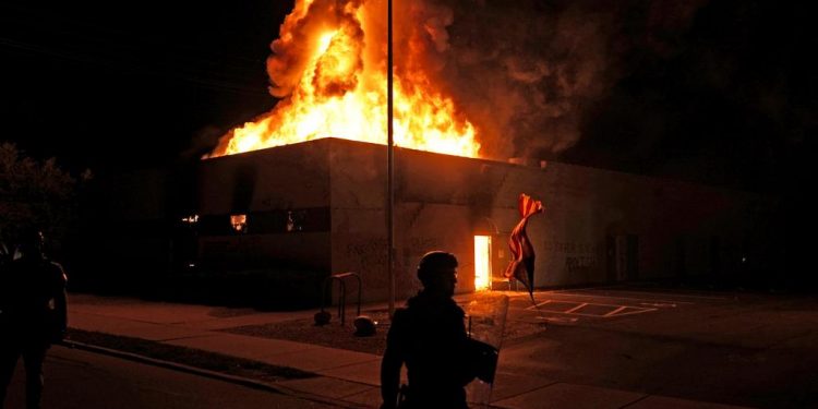 An American flag falls from its pole as police attempt to secure the area after protesters set fire to the department of corrections building, late Monday, Aug. 24, 2020, in Kenosha, Wis. Protests have erupted following the police shooting of Jacob Blake a day earlier. (AP Photo/David Goldman)